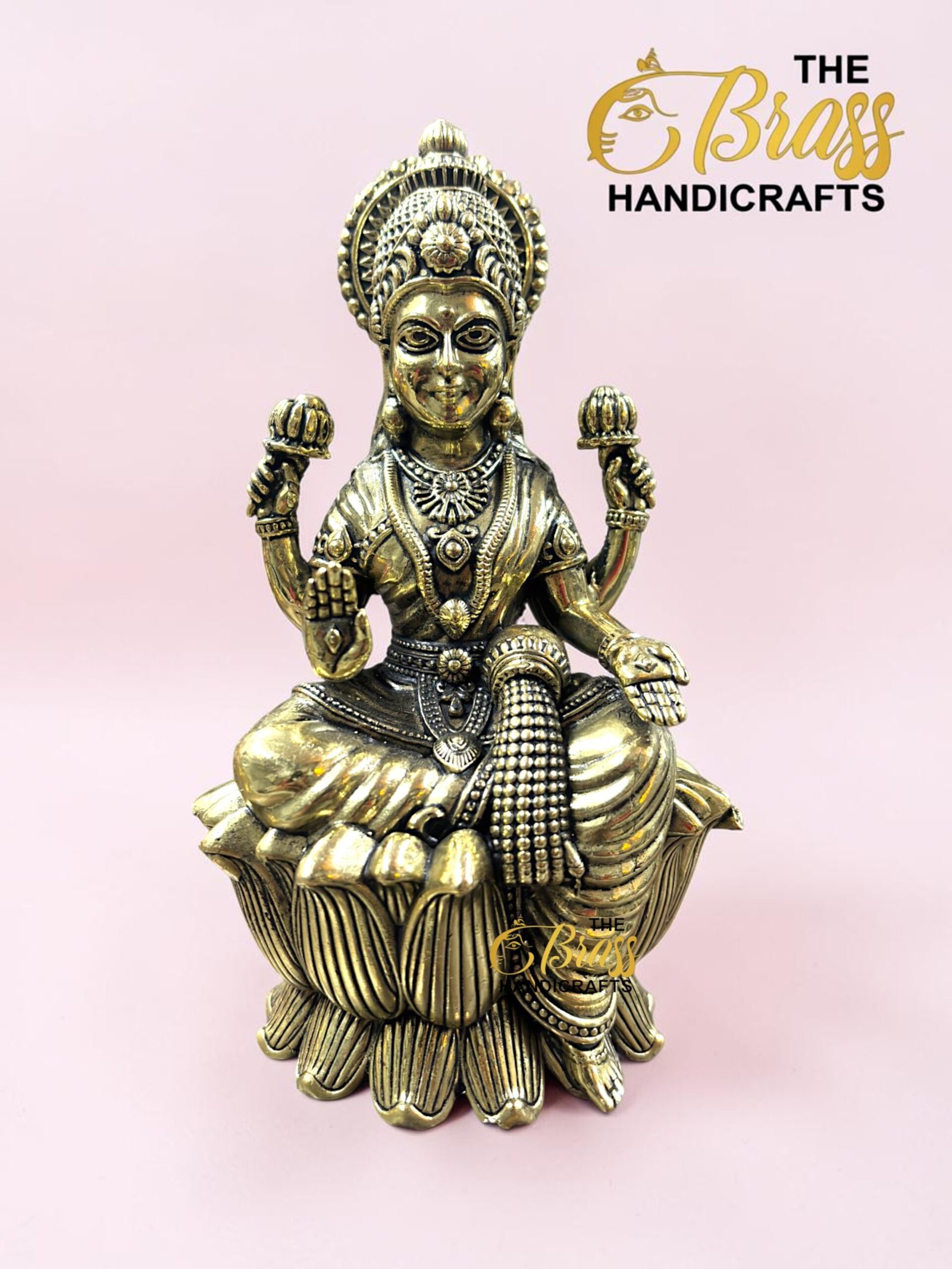 IMG_5776 - thebrasshandicrafts.com Brass statue of a Hindu goddess seated on a lotus with ornate headdress, against a pink background and logo reading 'The Brass Handicrafts'. thebrasshandicrafts.com