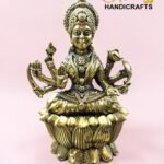 IMG_5779 - thebrasshandicrafts.com Gold-toned multi-armed deity statue with an ornate headdress, seated on a lotus pedestal against a pink background; branding for The Brass Handicrafts in the corner thebrasshandicrafts.com