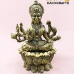 IMG_5780 - thebrasshandicrafts.com Gold brass deity statue with multiple arms and ornate headdress seated on a lotus base against a pink background; logo watermark reads 'The Brass Handicrafts'. thebrasshandicrafts.com