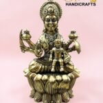 IMG_5781 - thebrasshandicrafts.com Brass goddess statue with child on a lotus base, pink background, logo reads The Brass Handicrafts. thebrasshandicrafts.com