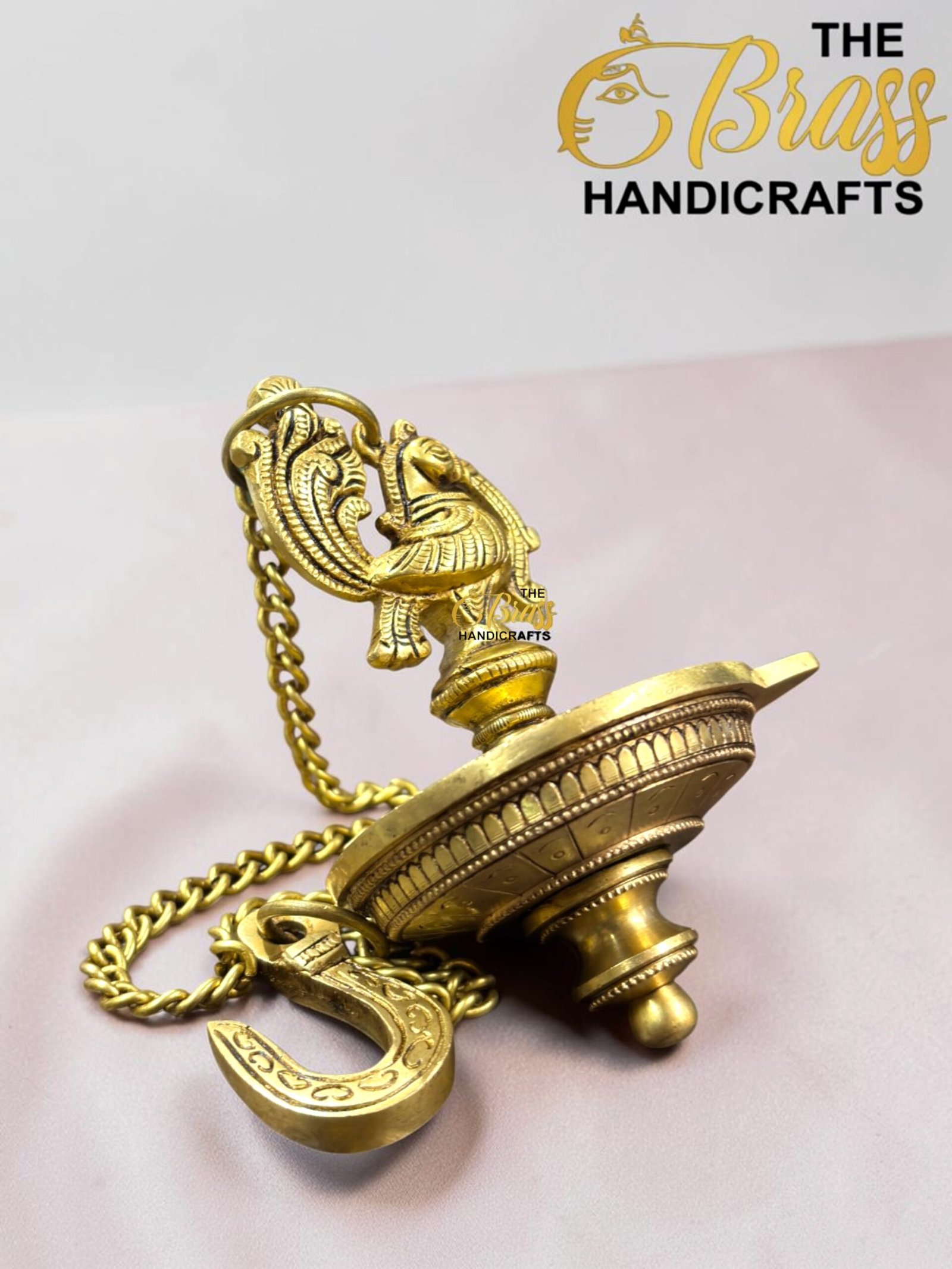 Close-up of an ornate gold pocket watch with a decorative chain on a pale pink surface.  thebrasshandicrafts.com
