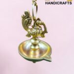 Ornate brass hanging lamp with a decorative bird-shaped finial, chain links, and a pink background.  thebrasshandicrafts.com