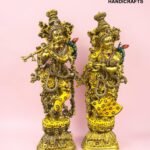 Pair of ornate gold brass statues adorned with colorful gems, set on decorative pedestals against a pink background; The Brass Handicrafts logo in the corner.  thebrasshandicrafts.com