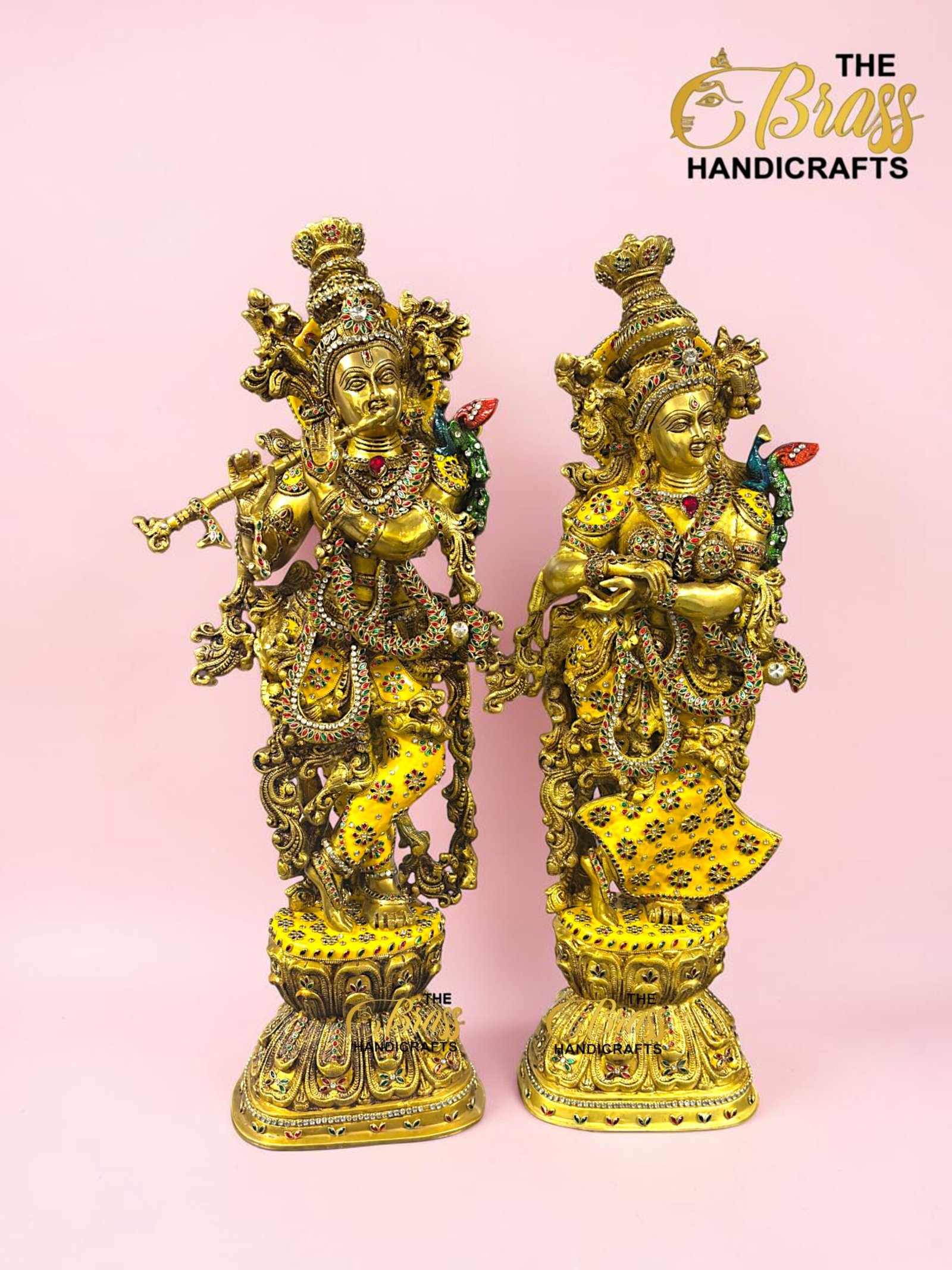 IMG_5921 - thebrasshandicrafts.com Pair of ornate gold brass statues adorned with colorful gems, set on decorative pedestals against a pink background; The Brass Handicrafts logo in the corner. thebrasshandicrafts.com
