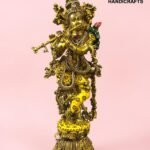 IMG_5922 - thebrasshandicrafts.com Gold-toned brass statue of a richly adorned Hindu deity, embellished with colorful gems, standing on a jeweled pedestal against a pink background (brand: The Brass Handicrafts). thebrasshandicrafts.com