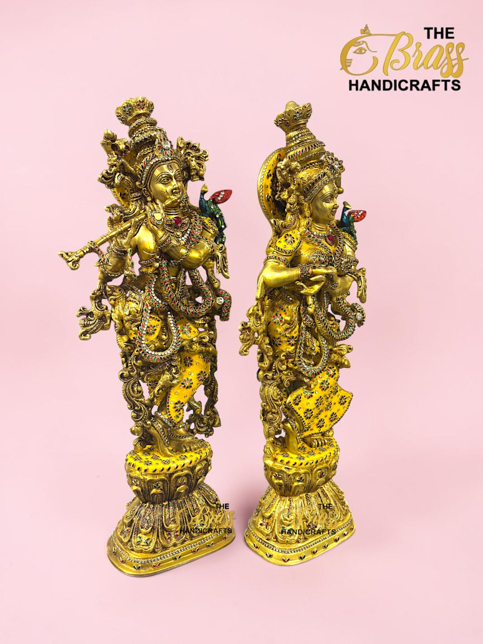 IMG_5925 - thebrasshandicrafts.com Two ornate gold brass statues adorned with colorful stones on decorative bases against a pink backdrop; The Brass Handicrafts logo in the corner. thebrasshandicrafts.com
