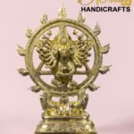 Gold brass Nataraja statue with a circular ornate ring on a pedestal, set against a pink background with 'The Brass Handicrafts' logo in the corner.  thebrasshandicrafts.com