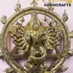 Gold brass statue of a multi-armed Hindu deity inside an ornate circular frame, on a pale pink background, with 'The Brass Handicrafts' logo visible.  thebrasshandicrafts.com