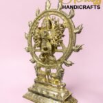Golden brass statue of Shiva Nataraja dancing inside a circular ornate ring on a decorative base, pink background.  thebrasshandicrafts.com
