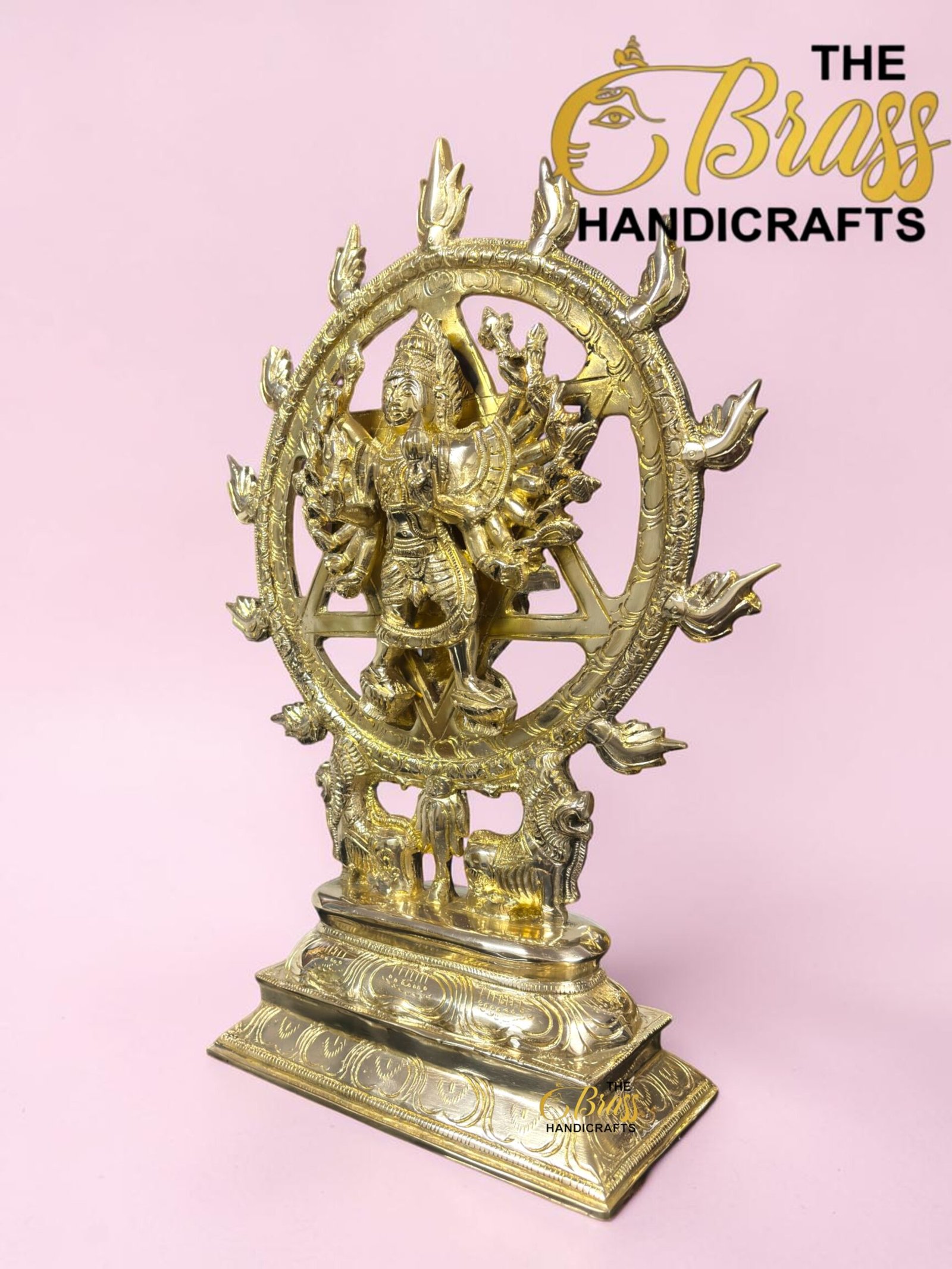 Golden brass statue of Shiva Nataraja dancing inside a circular ornate ring on a decorative base, pink background.  thebrasshandicrafts.com