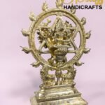 Ornate brass Nataraja statue (Shiva) dancing inside a circular ring, on a decorative pedestal with a pink background and 'The Brass Handicrafts' watermark.  thebrasshandicrafts.com