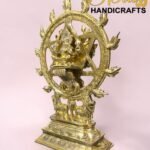 Gold-toned statue of Shiva Nataraja inside a flaming circular ring, with an ornate pedestal, set against a pink background.  thebrasshandicrafts.com