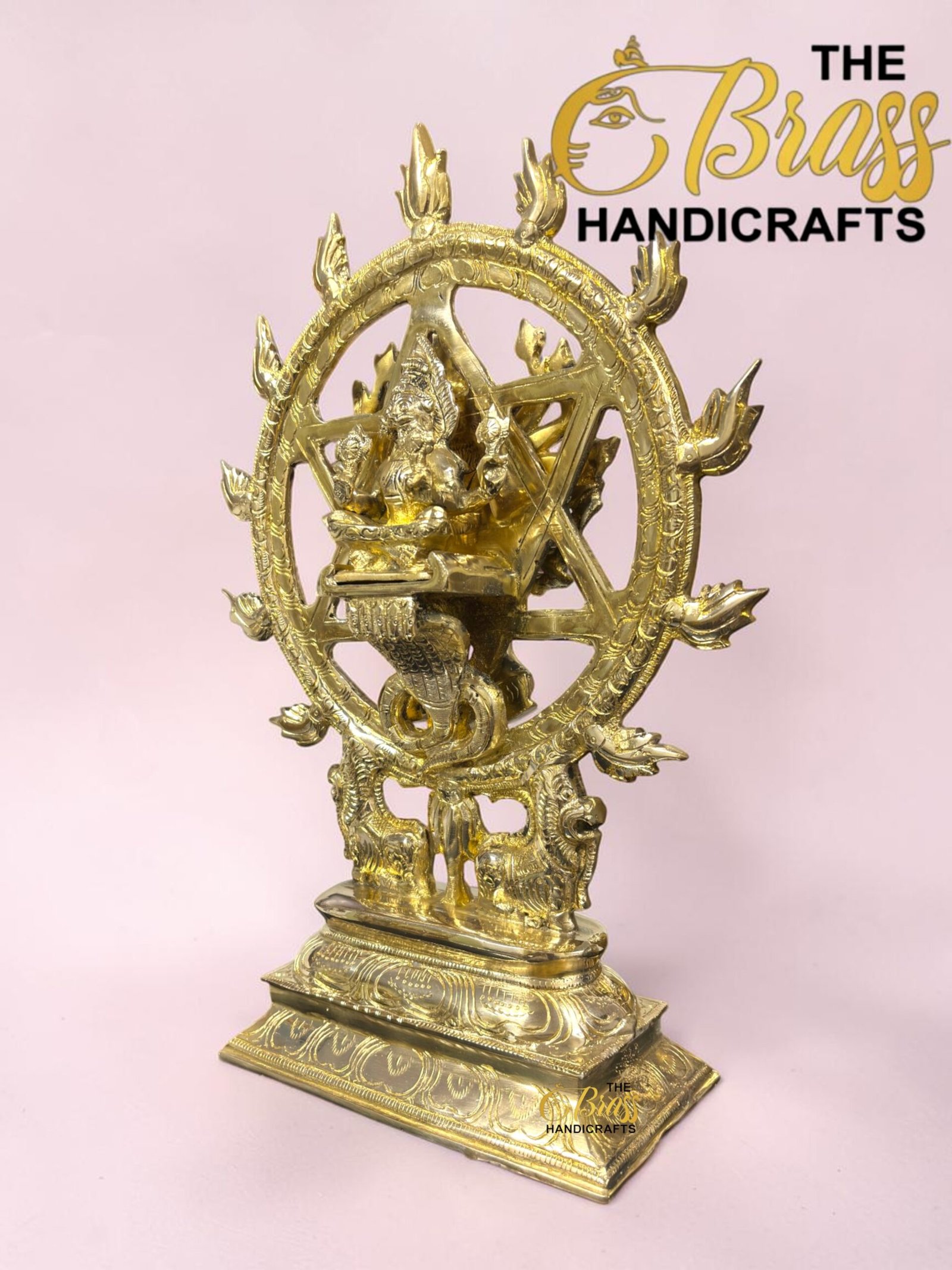 Gold-toned statue of Shiva Nataraja inside a flaming circular ring, with an ornate pedestal, set against a pink background.  thebrasshandicrafts.com