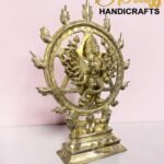 Gold Nataraja statue with a fiery circular ring, set on a decorative pedestal against a pink background.  thebrasshandicrafts.com
