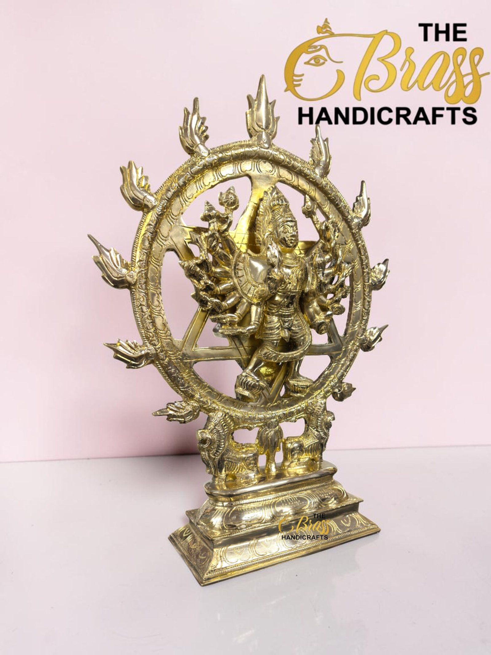 Gold Nataraja statue with a fiery circular ring, set on a decorative pedestal against a pink background.  thebrasshandicrafts.com