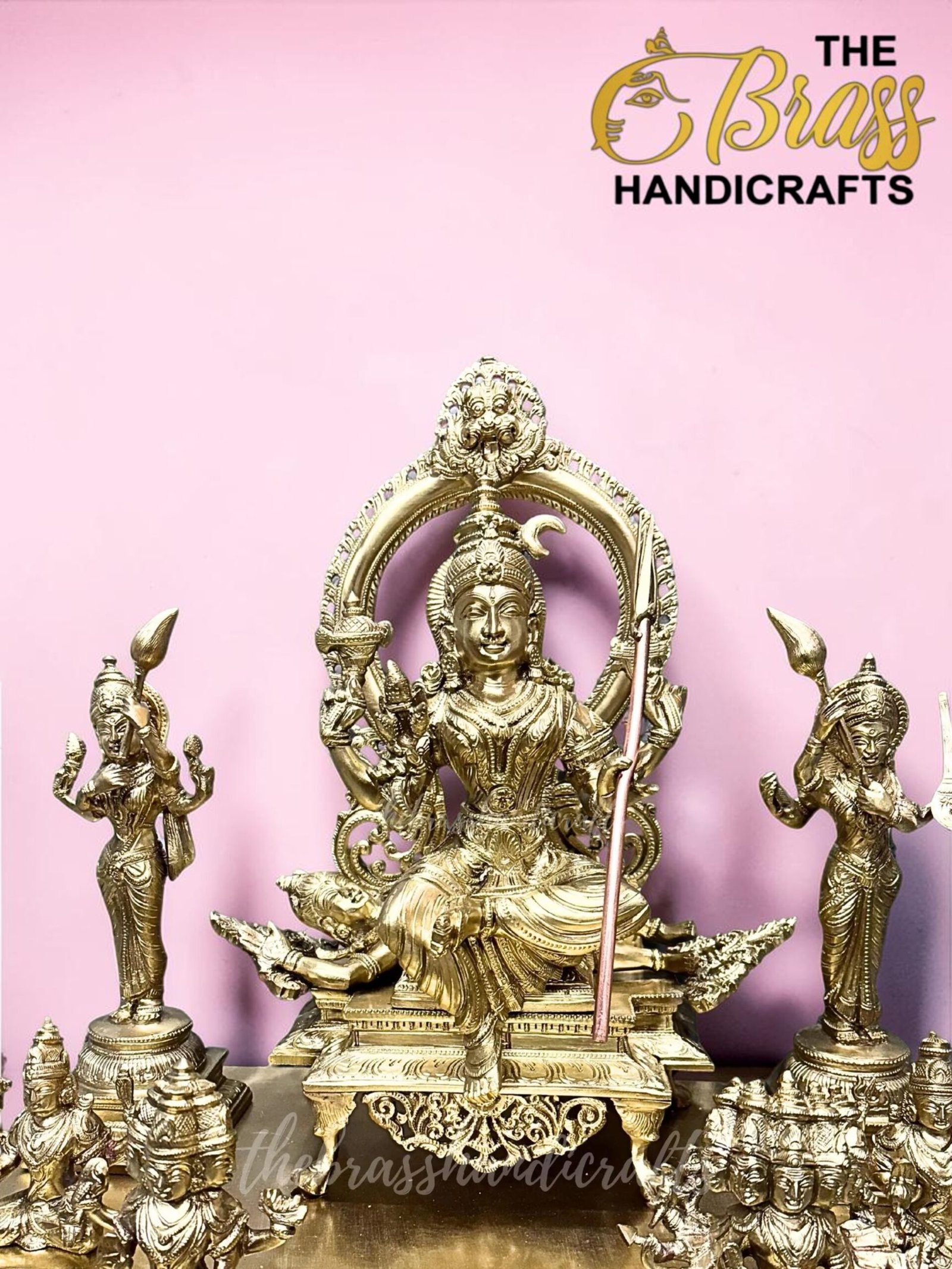Gold brass Hindu deity statue with smaller figures arranged around it, set against a pink backdrop.  thebrasshandicrafts.com