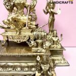 Intricately detailed gold-tone brass statues, with a central seated deity holding a staff and smaller figures around them against a pink backdrop.  thebrasshandicrafts.com