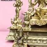 Gold brass Hindu statues arranged on a decorative pedestal against a pink background, with the 'The Brass Handicrafts' logo in the corner.  thebrasshandicrafts.com
