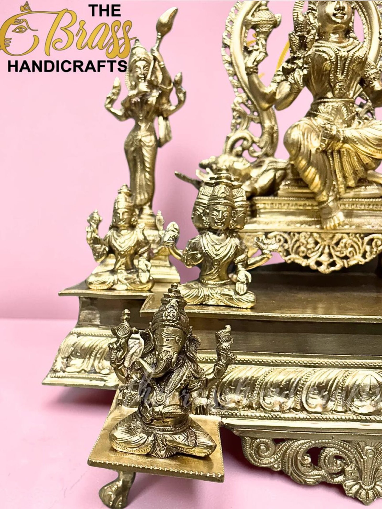 Gold brass Hindu statues arranged on a decorative pedestal against a pink background, with the 'The Brass Handicrafts' logo in the corner.  thebrasshandicrafts.com