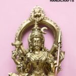 Ornate brass statue of a Hindu deity with a circular halo, set against a pink background.  thebrasshandicrafts.com