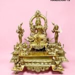 Gold brass Hindu deity statue with surrounding figures on an ornate pedestal, pink background.  thebrasshandicrafts.com