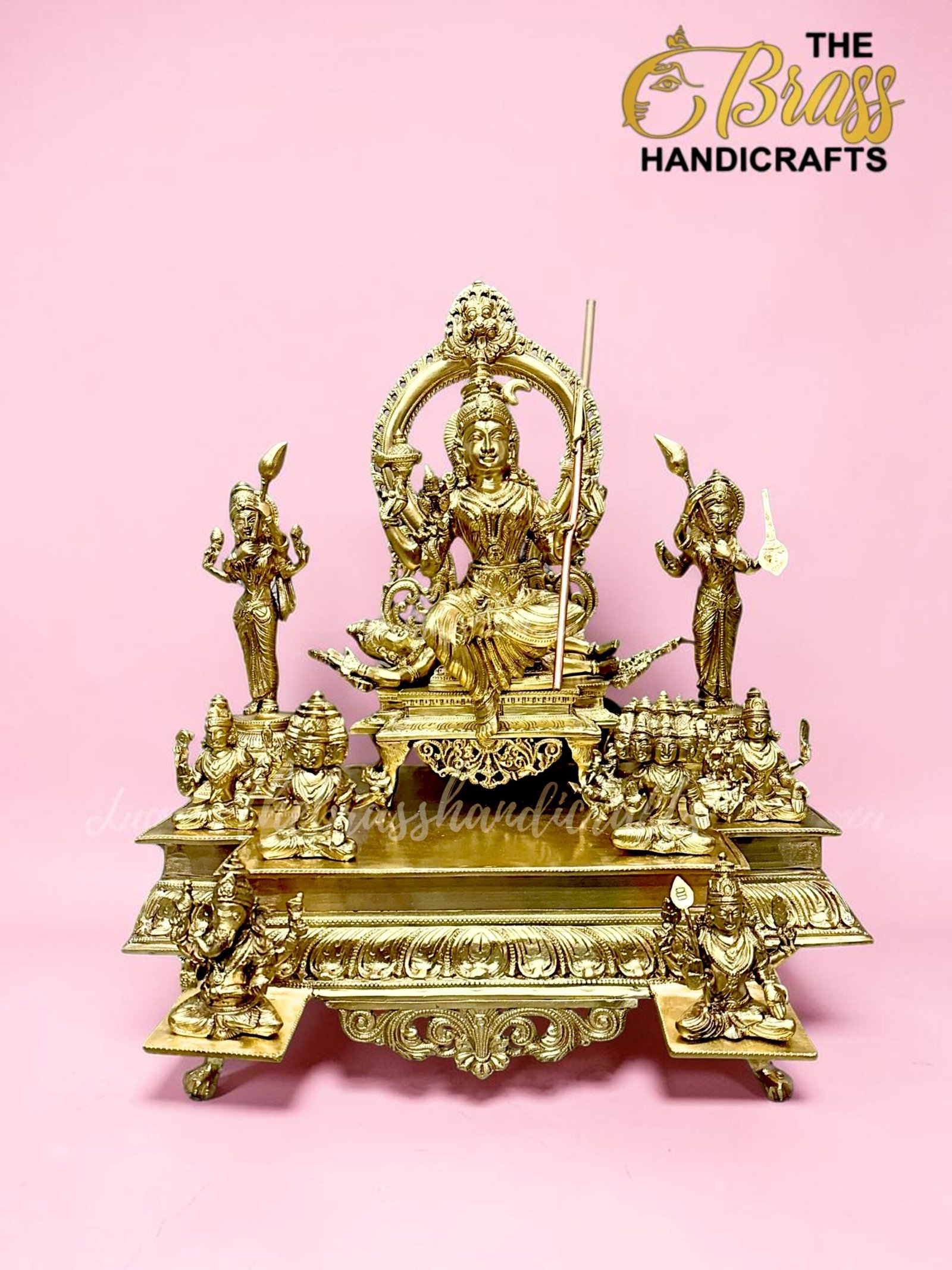 Gold brass Hindu deity statue with surrounding figures on an ornate pedestal, pink background.  thebrasshandicrafts.com