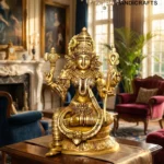 il_1588xN7607204836_ieyt - thebrasshandicrafts.com Golden Hindu deity statue with multiple arms on a pedestal, set in a luxurious living room with chandeliers and paintings in the background. thebrasshandicrafts.com
