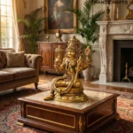 il_1588xN7655146347_7x2y - thebrasshandicrafts.com Golden ornate Hindu statue on a glass-topped coffee table in a luxurious room with antique furniture and a large framed portrait in the background, plus a logo. thebrasshandicrafts.com