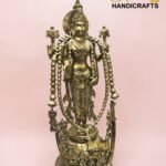 Brass statue of a multi-armed Hindu goddess with ornate jewelry, standing on a pedestal against a pink background.  thebrasshandicrafts.com