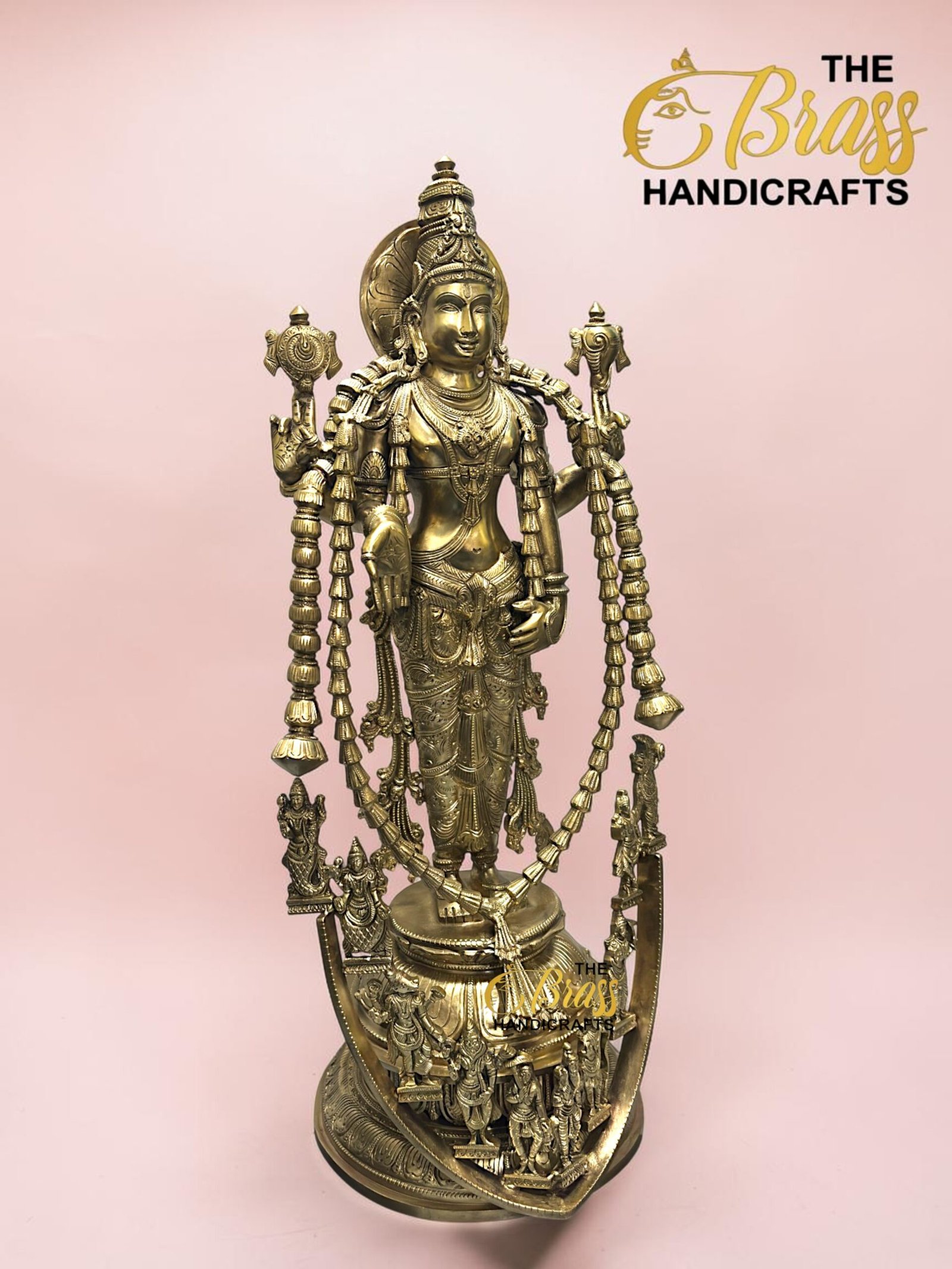 Brass statue of a multi-armed Hindu goddess with ornate jewelry, standing on a pedestal against a pink background.  thebrasshandicrafts.com