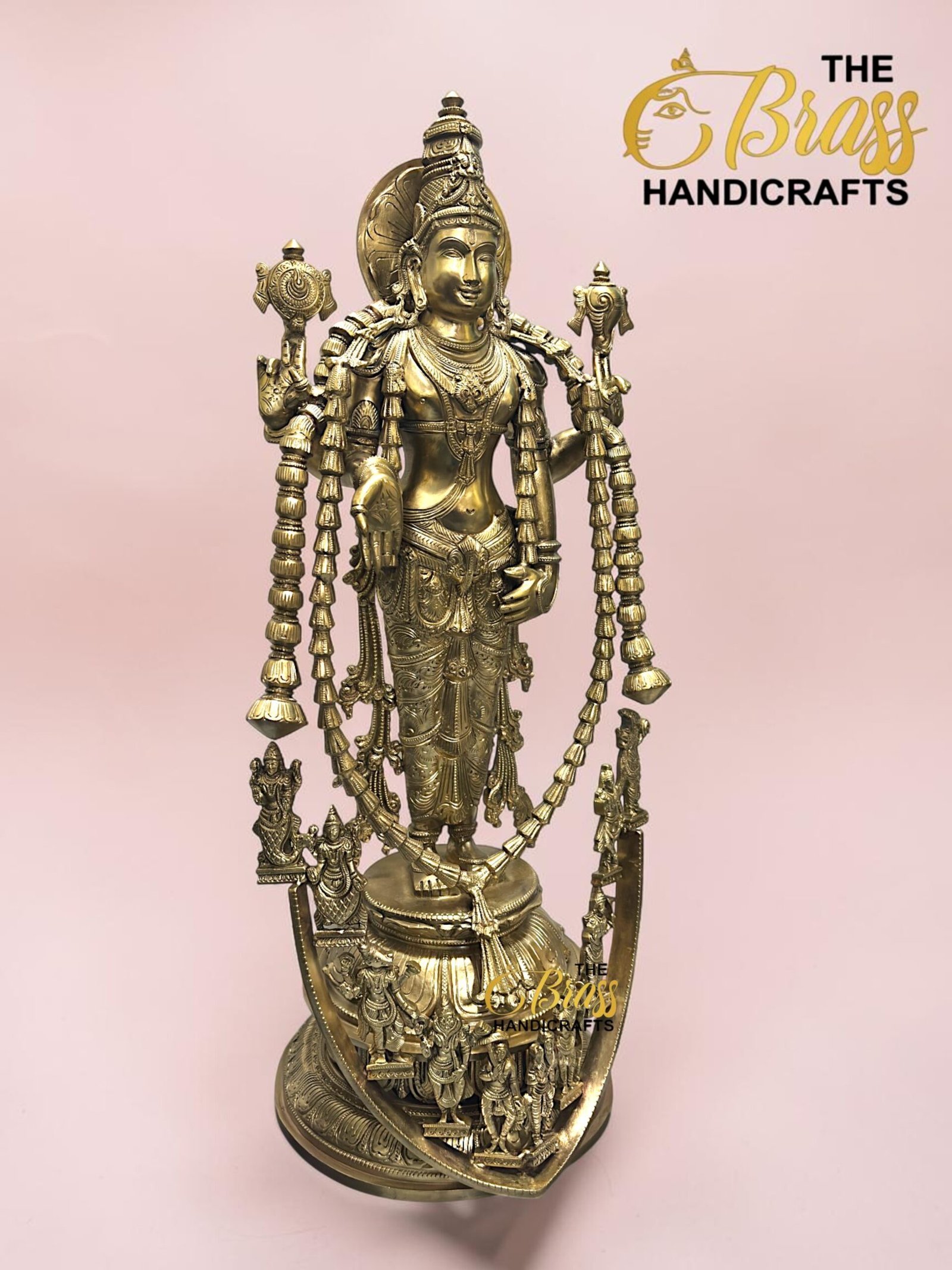 Golden ornate Hindu deity statue adorned with long bead garlands, pink background.  thebrasshandicrafts.com
