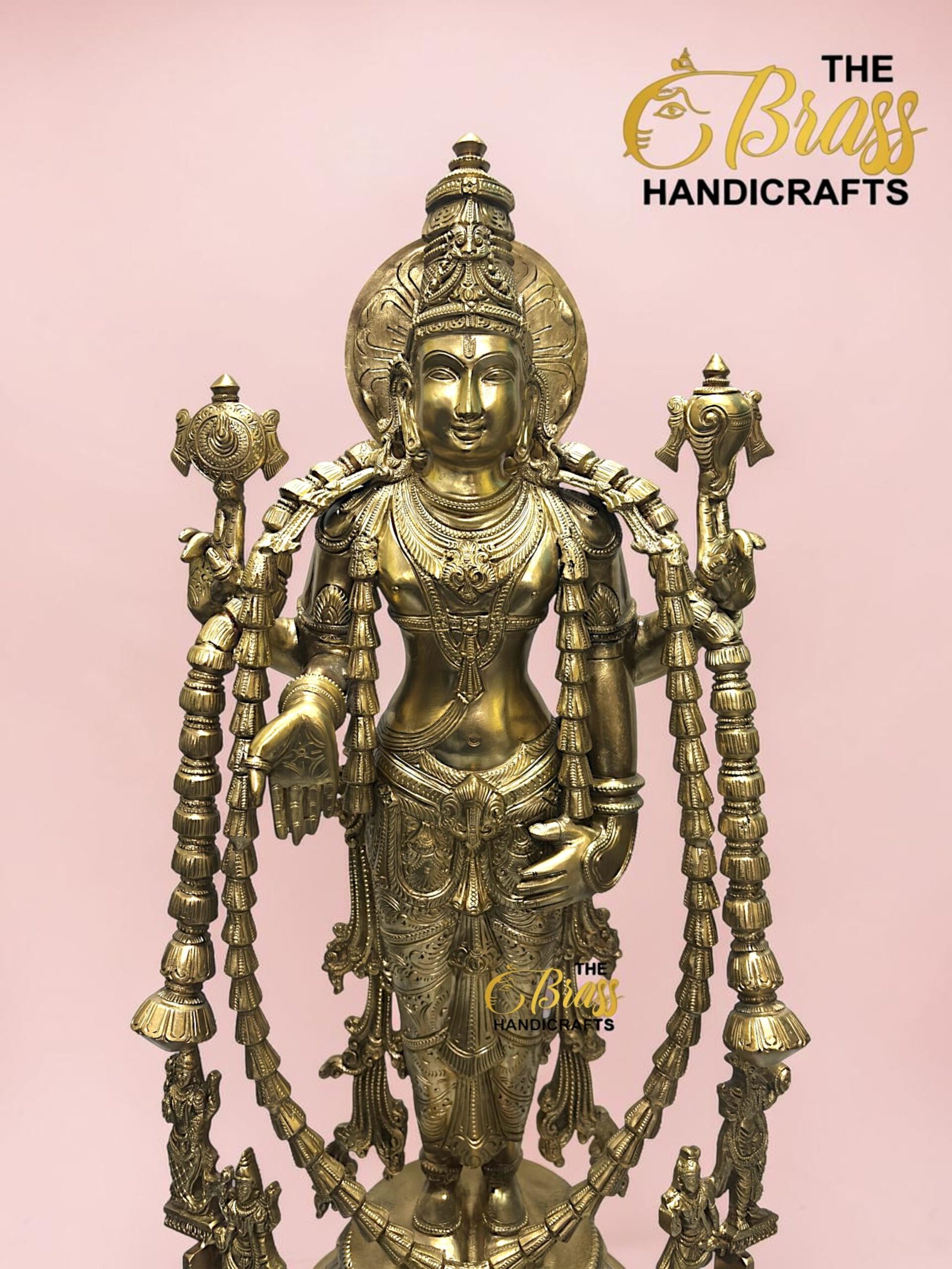 Golden multi-armed deity statue with ornate jewelry on a pink background; The Brass Handicrafts branding is visible.  thebrasshandicrafts.com