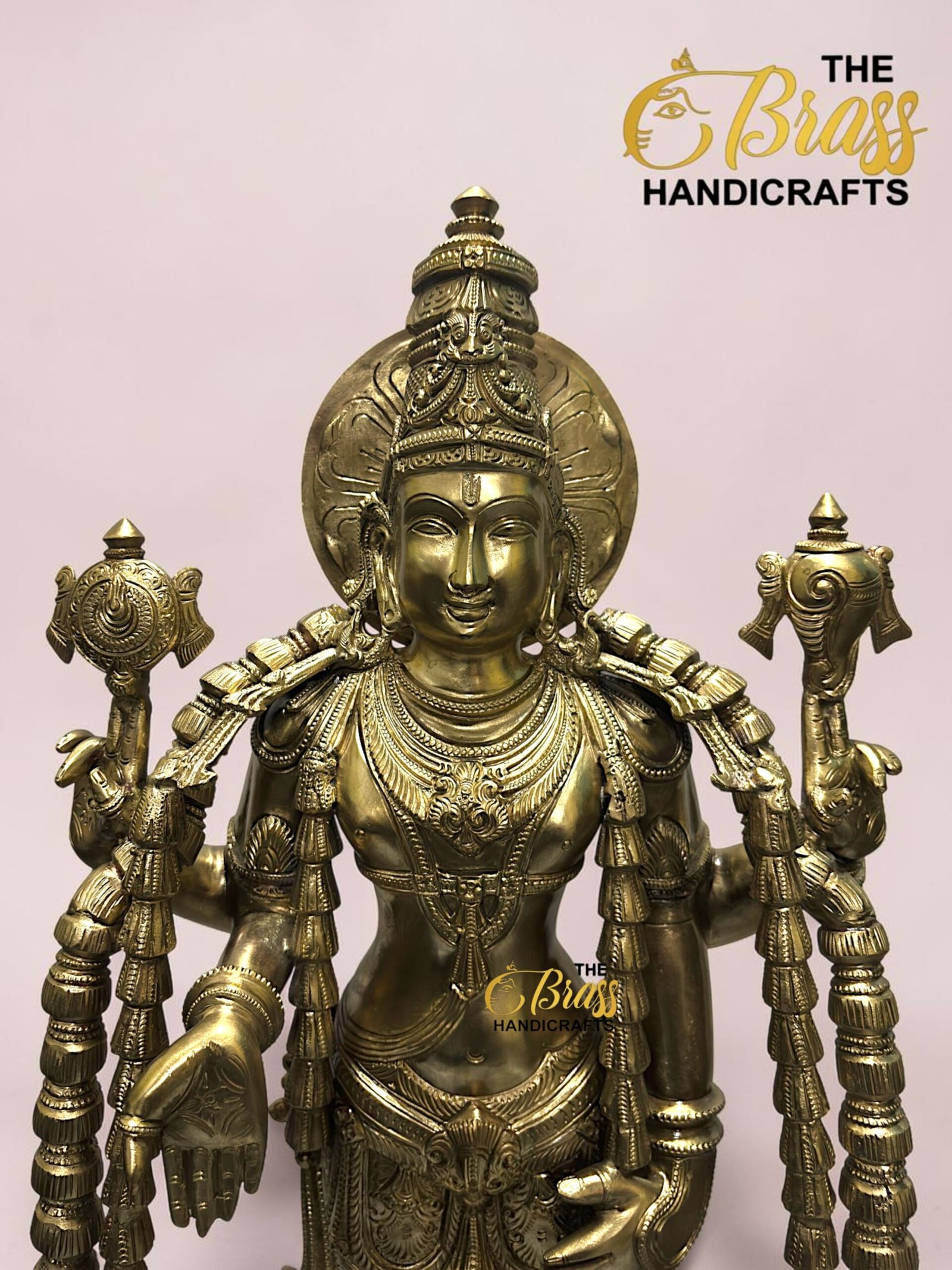 Gold brass statue of a multi-armed Hindu goddess with an ornate headdress, intricate jewelry, and ceremonial symbols, on a pale pink background. (Brand: The Brass Handicrafts)  thebrasshandicrafts.com