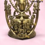 Intricately detailed brass Hindu deity statue with multiple figures, set against a pink background.  thebrasshandicrafts.com