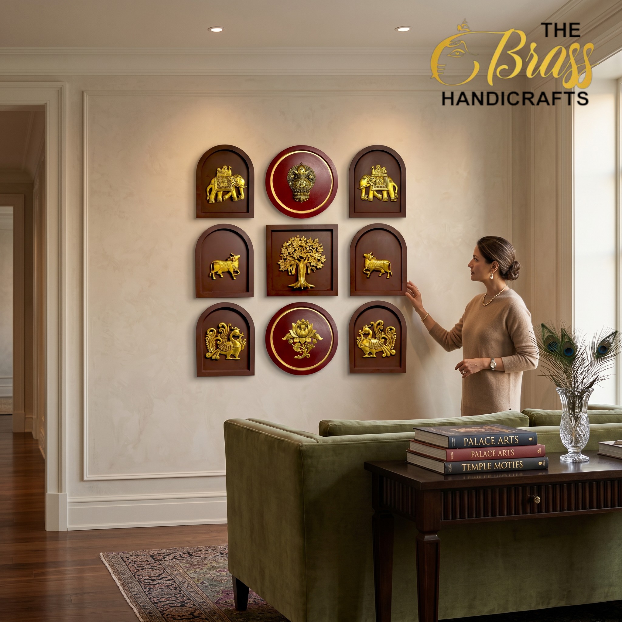 Wall with Indian-inspired gold plaque art featuring elephants and a central red round piece; a woman in beige touches a plaque on the right, with a peacock feather plant nearby.  thebrasshandicrafts.com