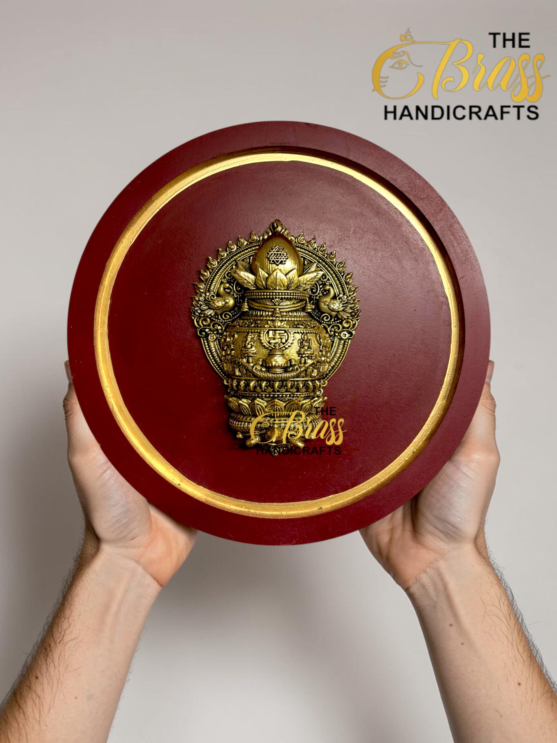 Round burgundy plaque with an ornate gold emblem being held, gold trim visible and a 'The Brass Handicrafts' watermark in the corner  thebrasshandicrafts.com