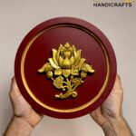 Red circular brass plaque with a gold lotus floral ornament being held by two hands; logo 'The Brass Handicrafts' appears in the upper corner.  thebrasshandicrafts.com