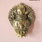 Intricately detailed gold brass ceremonial ornament with floral and swan motifs on a pink background; watermark reads 'The Brass Handicrafts'  thebrasshandicrafts.com
