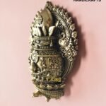 IMG_6163 - thebrasshandicrafts.com Ornate brass decorative sculpture with a crown-like top and intricate floral and geometric motifs against a pink background, branding visible at bottom right. thebrasshandicrafts.com