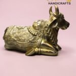 Gold decorative cow statue with intricate patterns on a pink background; 'The Brass Handicrafts' logo in the corner.  thebrasshandicrafts.com