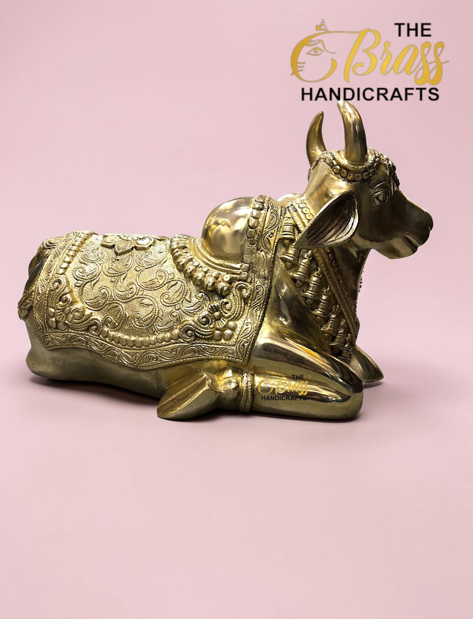 Gold decorative cow statue with intricate patterns on a pink background; 'The Brass Handicrafts' logo in the corner.  thebrasshandicrafts.com