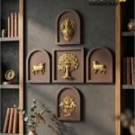 panch tatva 1 - thebrasshandicrafts.com Decorative wall display of gold bas-relief panels in brown frames on a gray wall, flanked by wooden shelves with books and pottery. thebrasshandicrafts.com