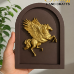 Gold Pegasus relief mounted on a brown arched plaque, held by a hand; The Brass Handicrafts branding in the corner.  thebrasshandicrafts.com