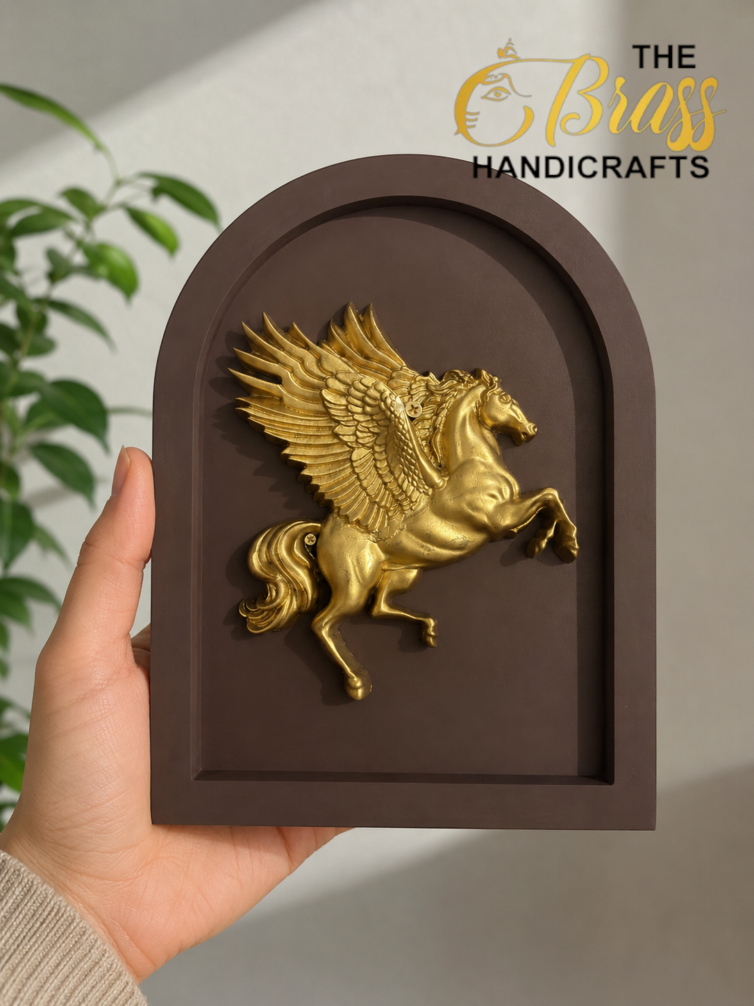 Gold Pegasus relief mounted on a brown arched plaque, held by a hand; The Brass Handicrafts branding in the corner.  thebrasshandicrafts.com