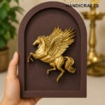 Hand holds a brown arched plaque with a gold Pegasus relief.  thebrasshandicrafts.com