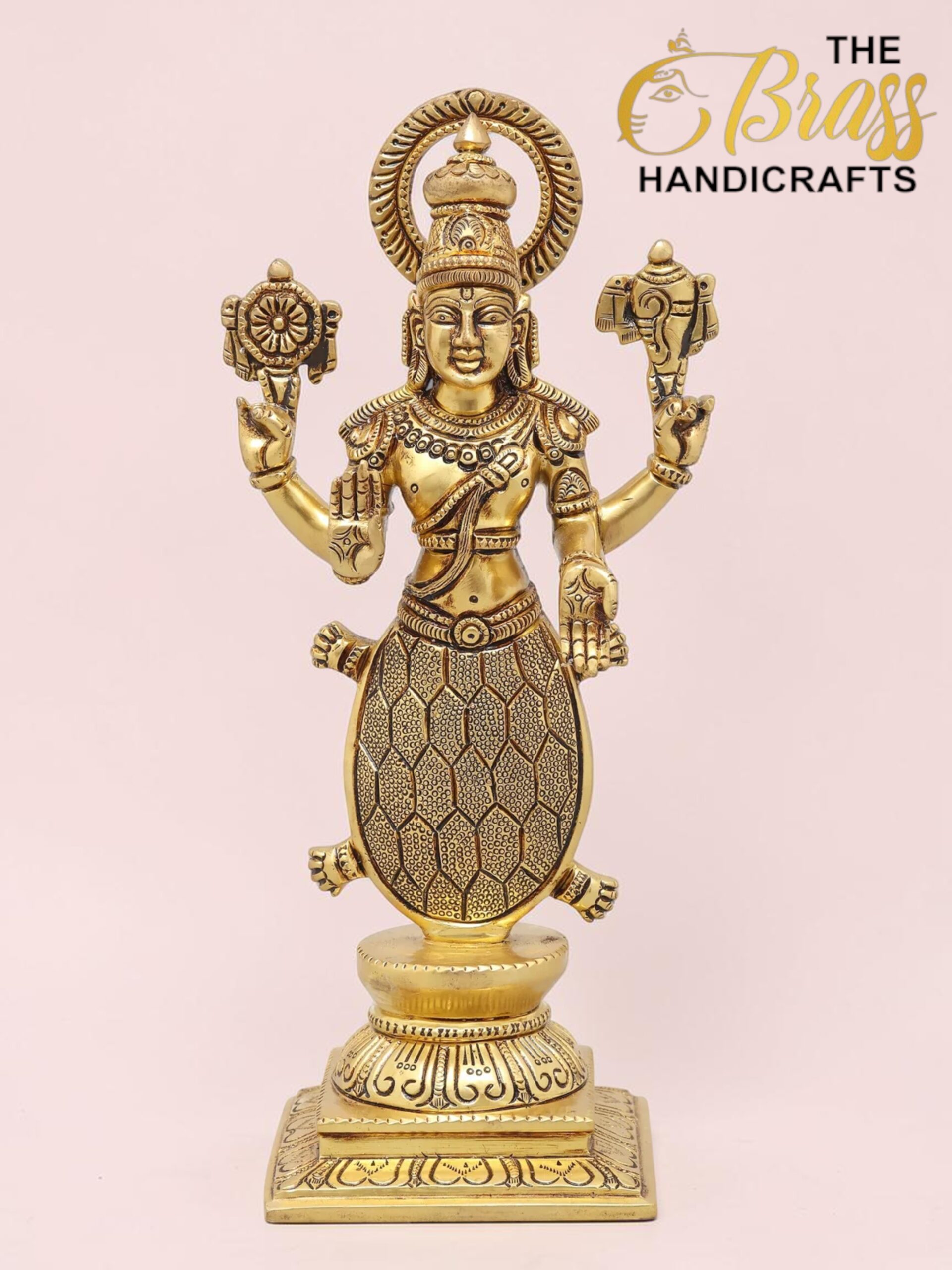 Brass statuette of the Hindu goddess Lakshmi standing on a base, with multiple arms and a lotus held in one hand, set against a pink background.  thebrasshandicrafts.com