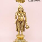 Gold-colored brass statue of a Hindu deity standing on a decorative pedestal, holding an umbrella aloft and a vessel in one hand, with intricate jewelry and detailing.  thebrasshandicrafts.com
