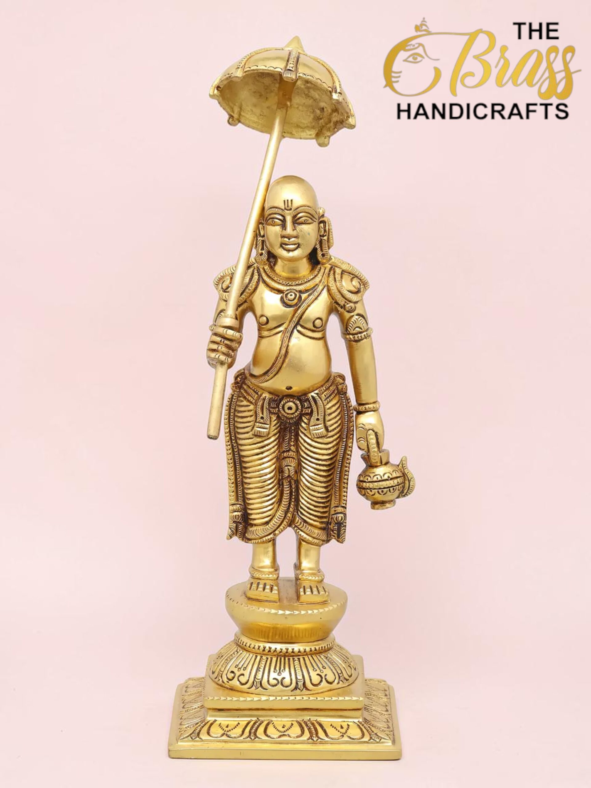Gold-colored brass statue of a Hindu deity standing on a decorative pedestal, holding an umbrella aloft and a vessel in one hand, with intricate jewelry and detailing.  thebrasshandicrafts.com