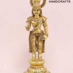 Gold statue of a Hindu deity with an ornate crown and halo, standing on a decorative base against a pink background; logo 'The Brass Handicrafts' visible in corner.  thebrasshandicrafts.com