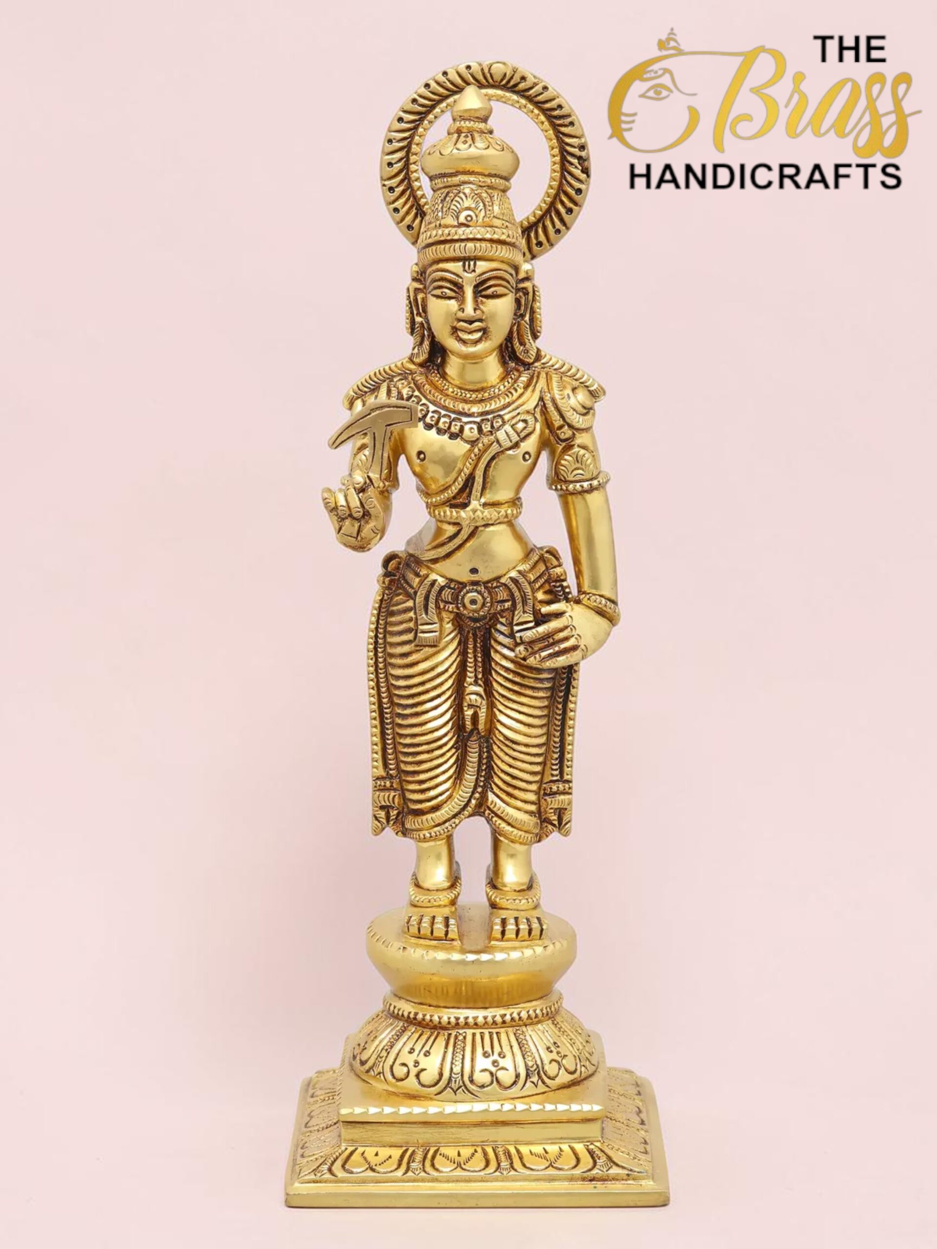 Gold statue of a Hindu deity with an ornate crown and halo, standing on a decorative base against a pink background; logo 'The Brass Handicrafts' visible in corner.  thebrasshandicrafts.com